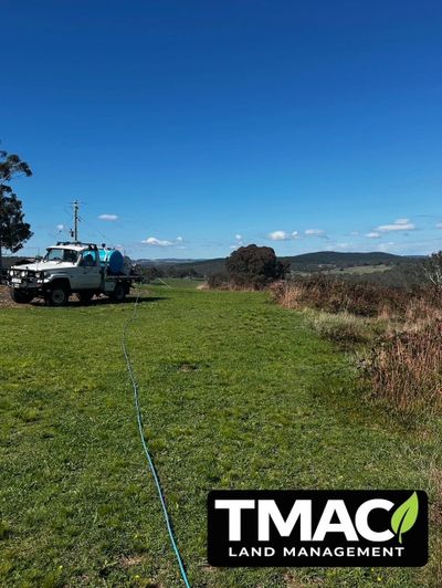 A truck on a grassy field with clear blue skies and TMAC Land Management logo.