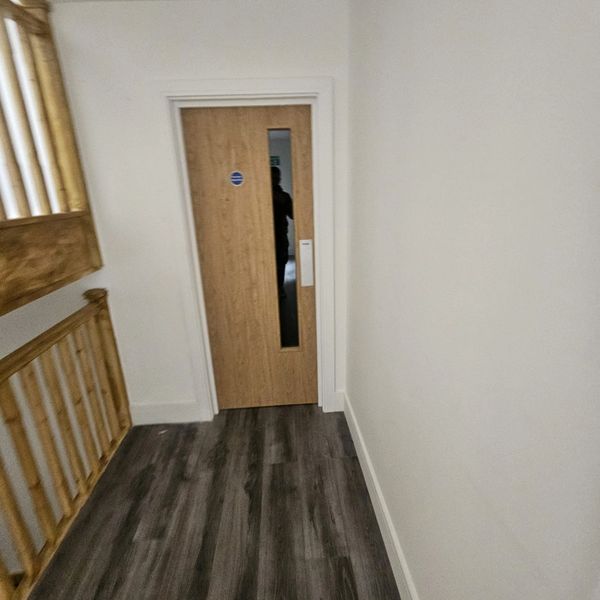 Hallway with wooden door and railing, dark wood floor.