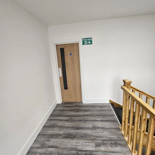 Hallway with wooden door labeled fire exit and wooden staircase railing.
