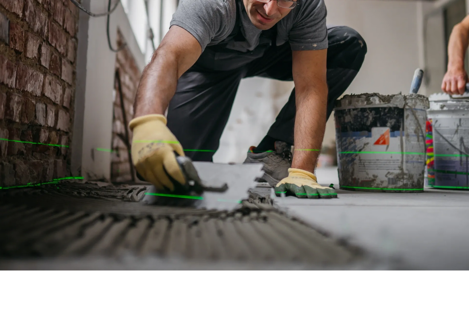 Worker spreading mortar on the floor near a brick wall with a trowel.