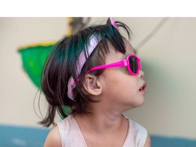 A young child wearing hearing aids and pink sunglasses. 