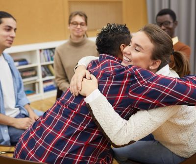 Two people, in a group of people sitting, are hugging. 
