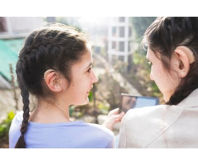 Two girls wearing hearing aids are smiling at each other. 