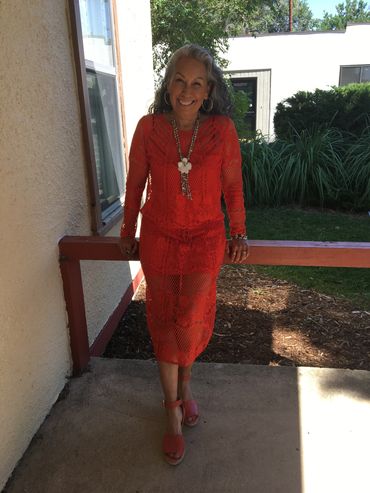Woman smiling in a bright orange dress on a sunny day.