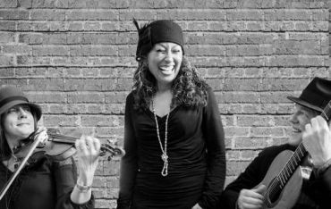 Three musicians performing by a brick wall.