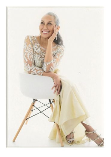 Elegant older woman smiling while seated on a chair.