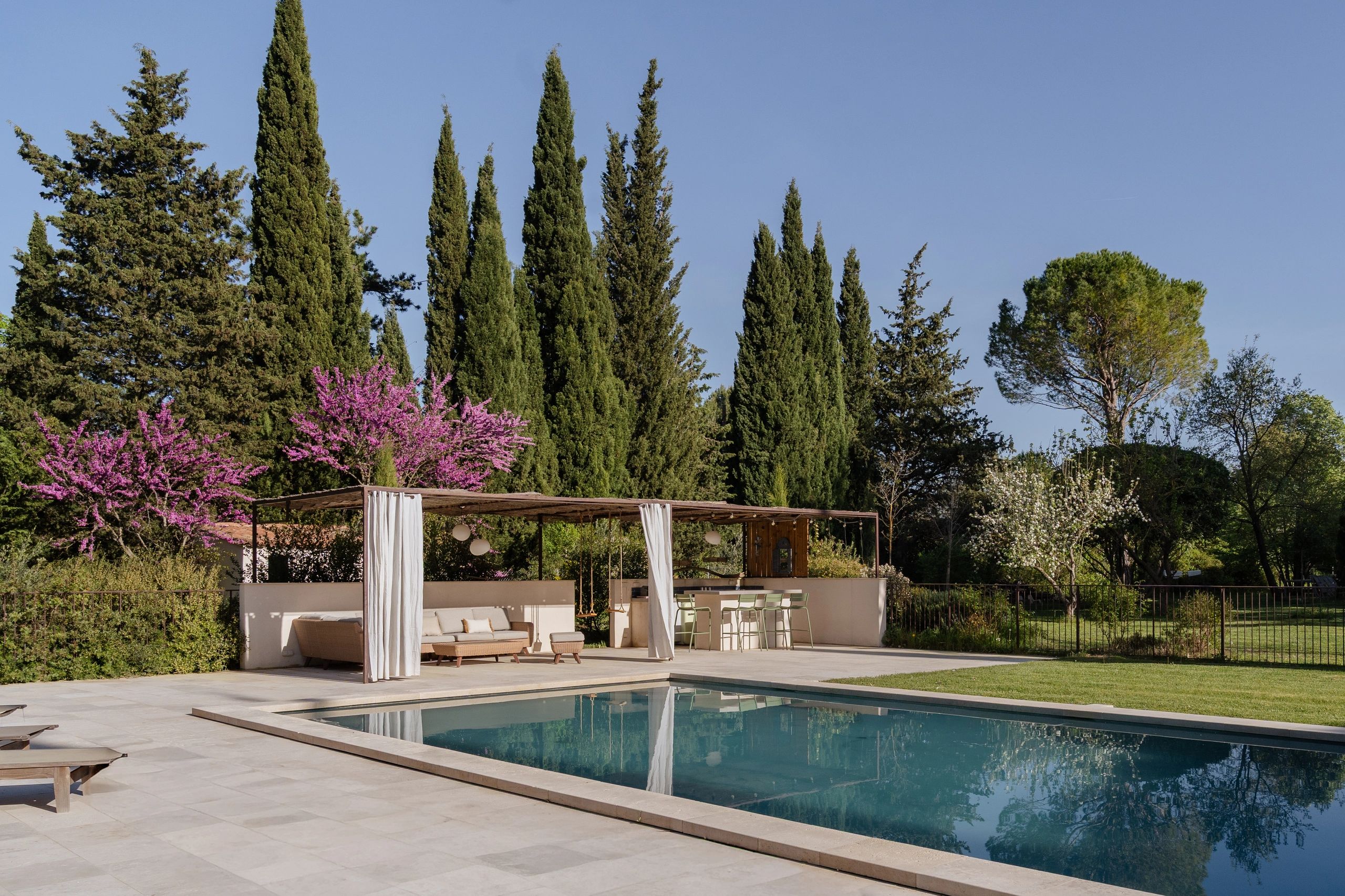 Modern outdoor pool area with seating and pergola surrounded by trees.