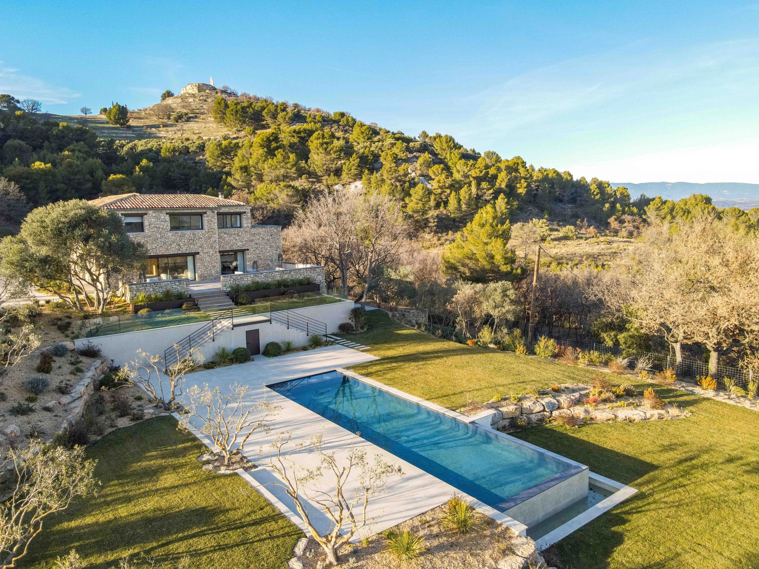 Stone house with a long pool in a lush mountainous landscape.
