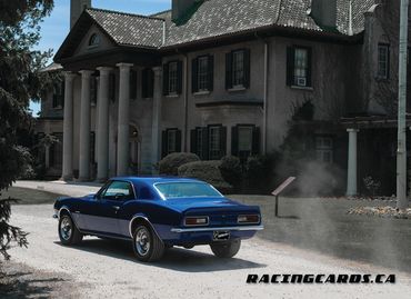 Blue classic muscle car parked in front of a historic mansion with columns.
