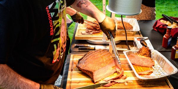 Person slicing smoked brisket on a wooden cutting board outdoors.