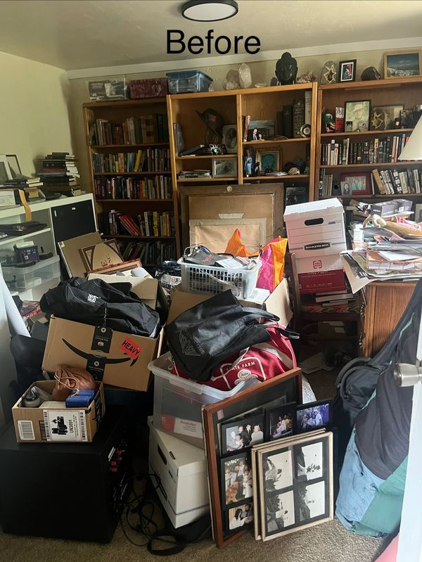 Cluttered room full of boxes, bags, and furniture.