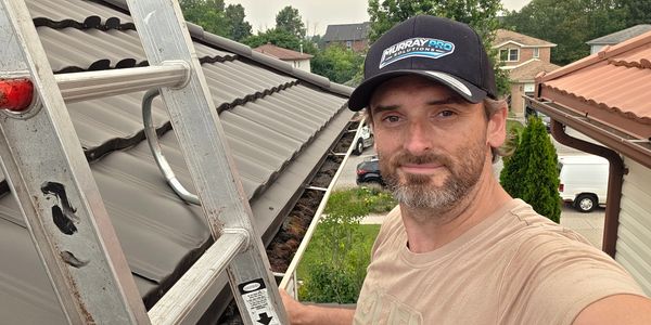 Man on ladder cleaning gutters wearing a Murray Pro Solutions cap.
