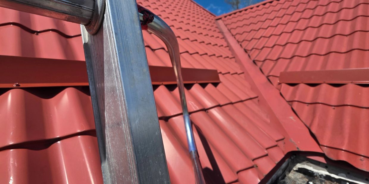 Close-up of a metal ladder on a red tiled roof under a clear blue sky.