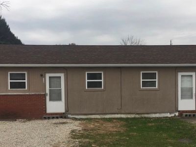 Simple single-story building with two white doors and three windows under a cloudy sky.
