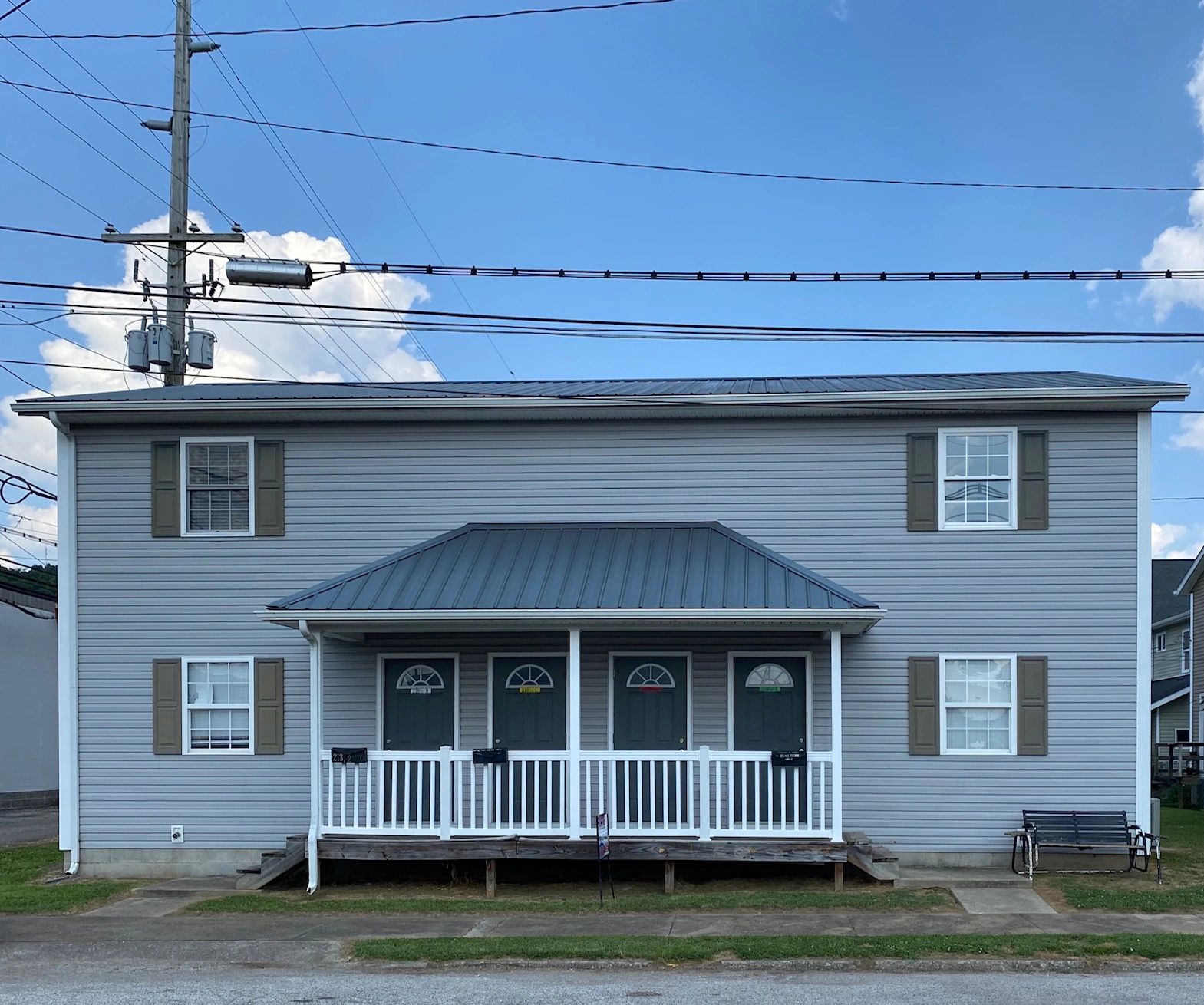 A duplex with four front doors and a small porch under a clear blue sky.