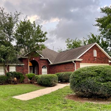 A cozy brick house with a well-maintained garden and cloudy sky.