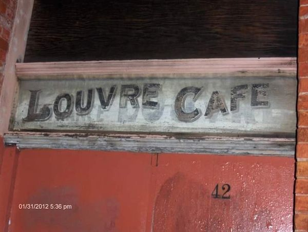 Faded sign of Louvre Cafe above a red door numbered 42.