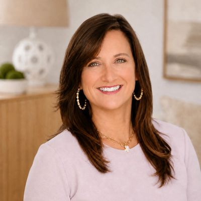 Woman with brown hair smiling, wearing hoop earrings and a light purple top.