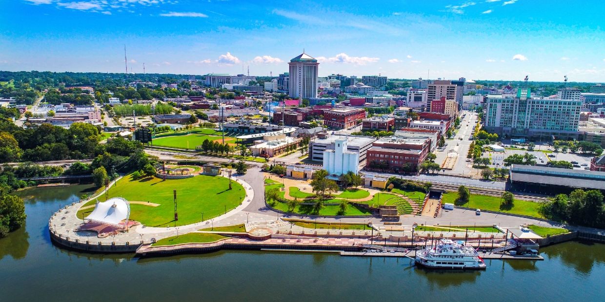 A city waterfront park with a boat docked and tall buildings in the background.