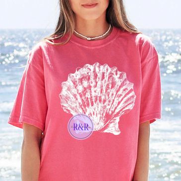Woman wearing a pink t-shirt with a large white seashell design at the beach.