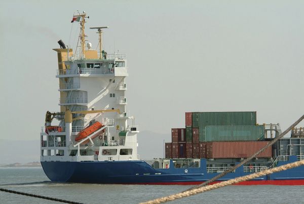 Cargo ship carrying stacked shipping containers on calm water.