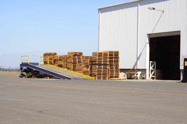 Stacks of wooden pallets outside a warehouse with a loading ramp.