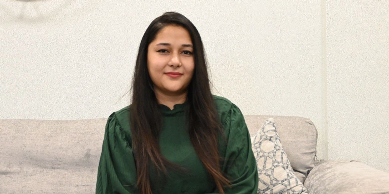 Woman sitting on a couch smiling, wearing a green top.