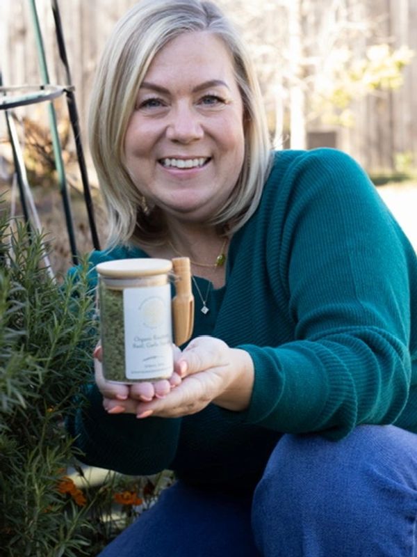 Smiling woman holding a jar of organic herb garden seeds outdoors.
