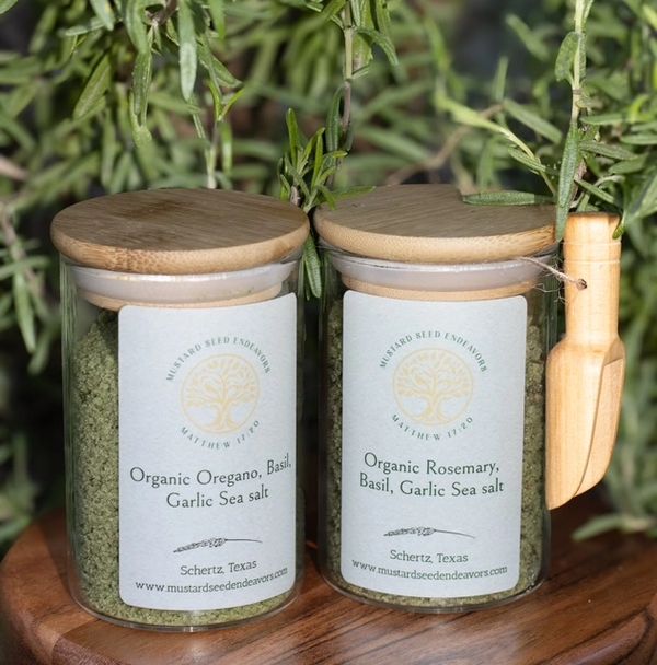 Glass jars of organic herb and garlic sea salt with wooden lids and scoop.