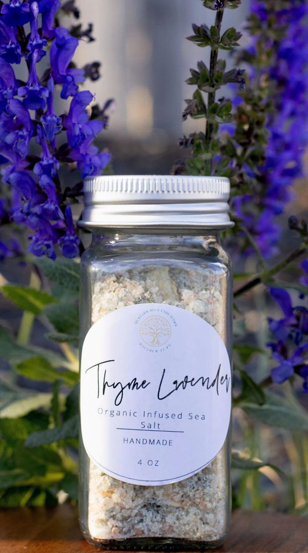 Jar of thyme lavender infused sea salt surrounded by purple flowers.
