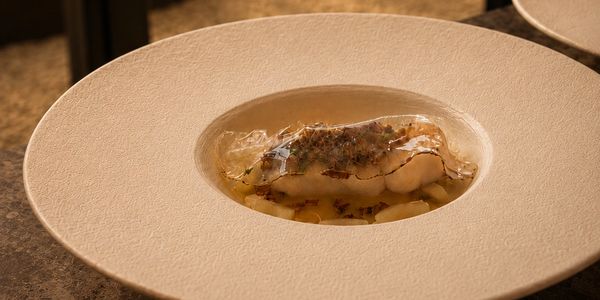 Gerecht met vis en doorzichtige saus in een witte kom.