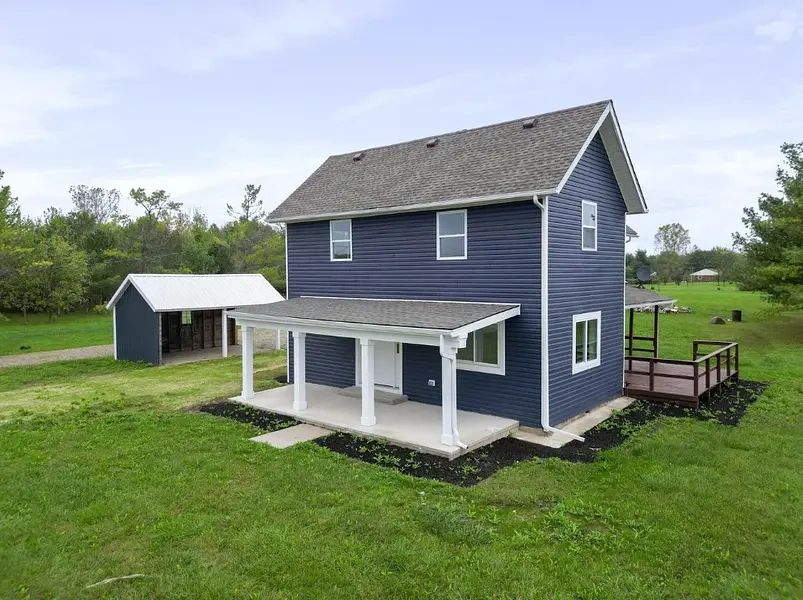 Blue two-story house with white porch and detached garage on a green lawn.