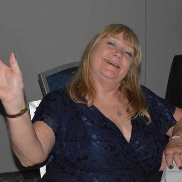 Smiling woman waving while seated at a table.
