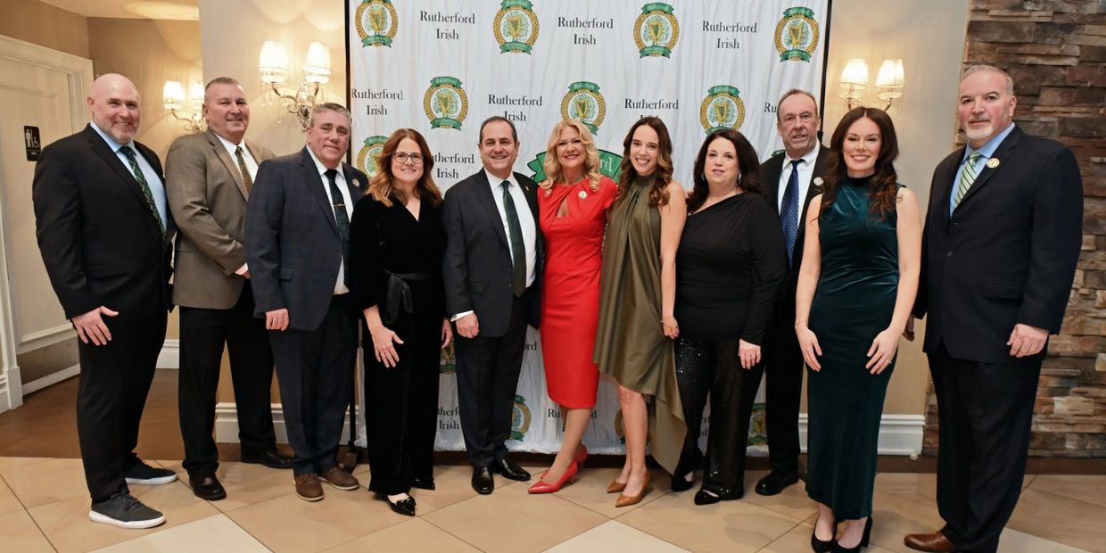 Group of twelve people dressed formally, posing at Rutherford Irish event.