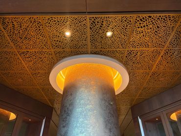 Laser-cut aluminum ceiling panels with a decorative pattern around a lit column, hotel remodel proje