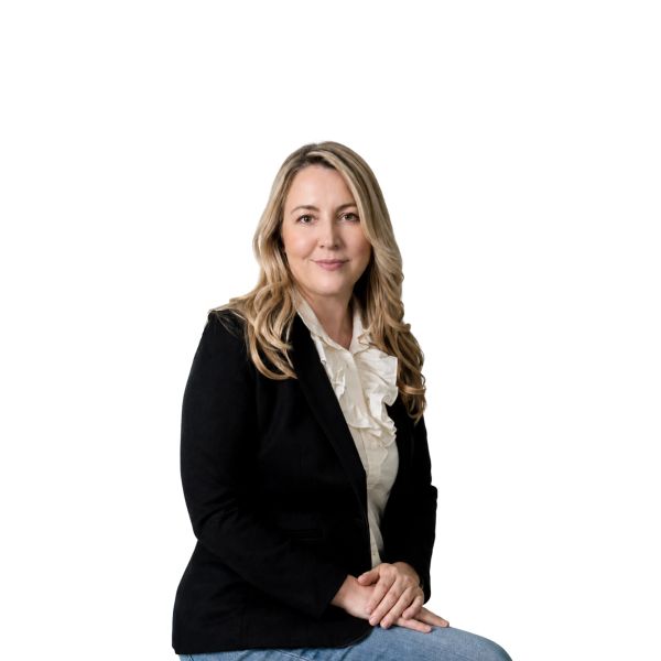Professional woman in a black blazer and ruffled white blouse sitting confidently.