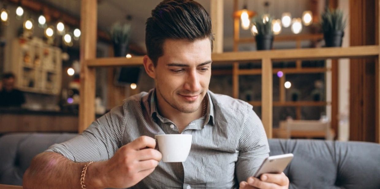 Man drinking coffee while looking at phone in a cafe.
