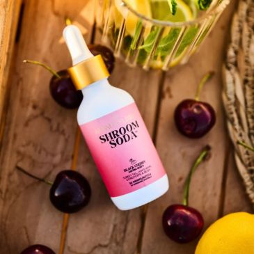 Shroom Soda skincare serum bottle surrounded by cherries and lemon.