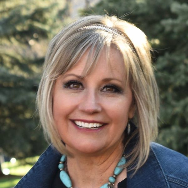 Smiling woman outdoors with short blonde hair and turquoise necklace.