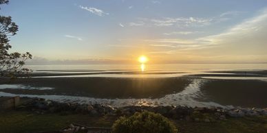 Sunset over a calm beach with clear skies and scattered clouds.