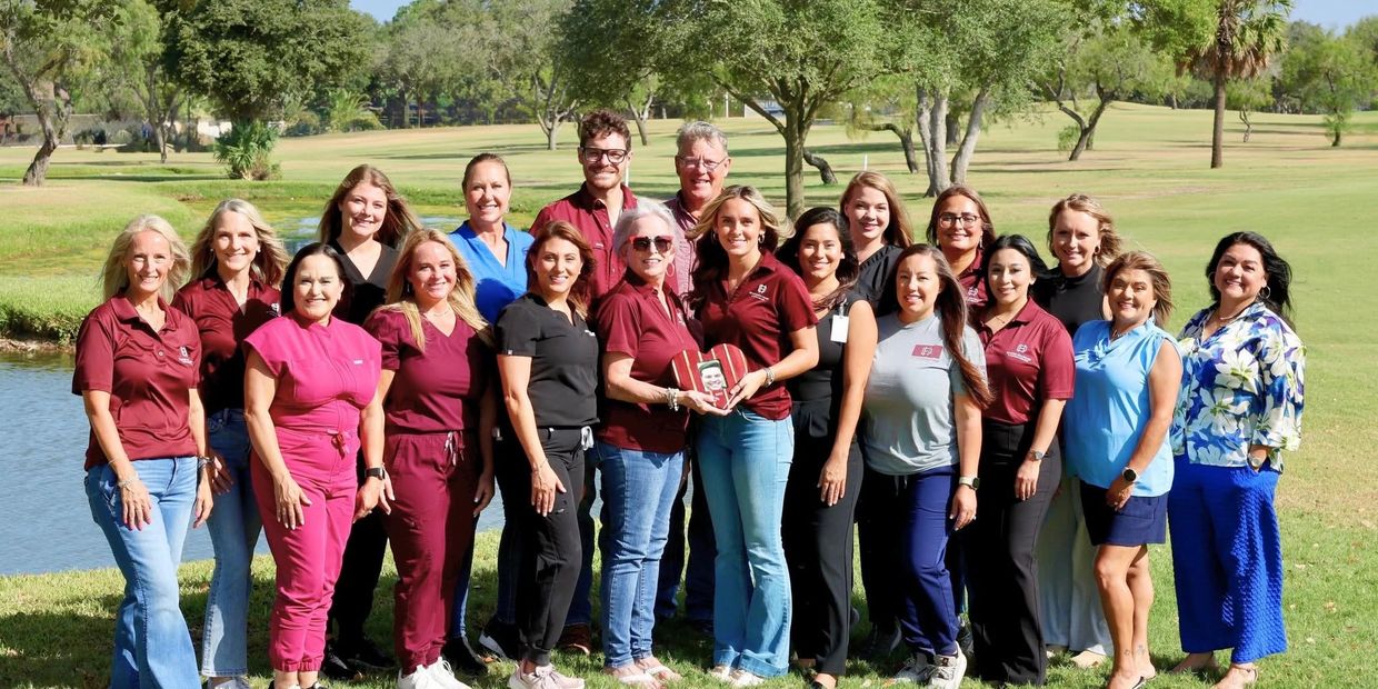 Group photo of smiling people outdoors near water and trees.