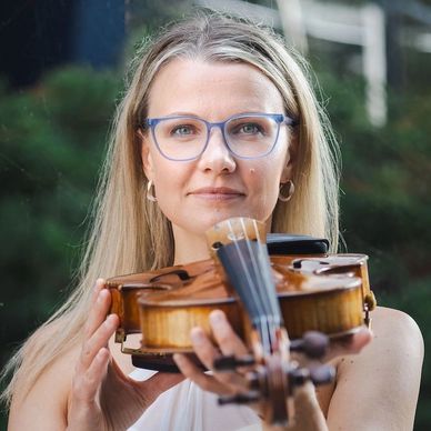 Woman holding a violin, looking at the camera.