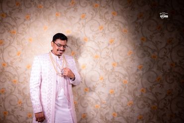 A man in traditional attire smiles, adjusting pearl necklaces.