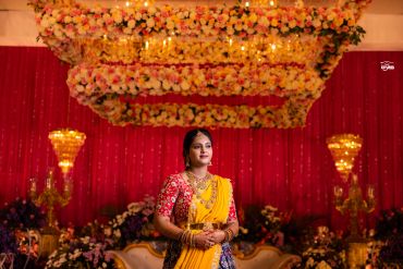 Woman in a yellow saree at a decorated event.