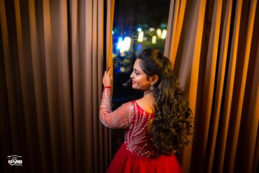 Woman in a red dress opening curtains at night.