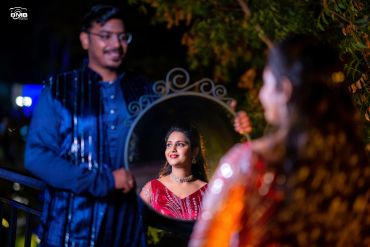 Man holding mirror reflecting smiling woman in red dress.