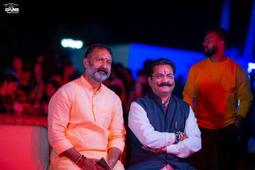 Two men sitting together at an event with colorful lighting.