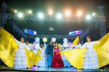 Couple posing with performers holding golden wings and lanterns on stage.