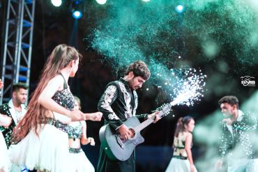 Musician playing guitar with pyrotechnics at a lively event.