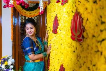 Woman in traditional attire beside a decorated flower wall.